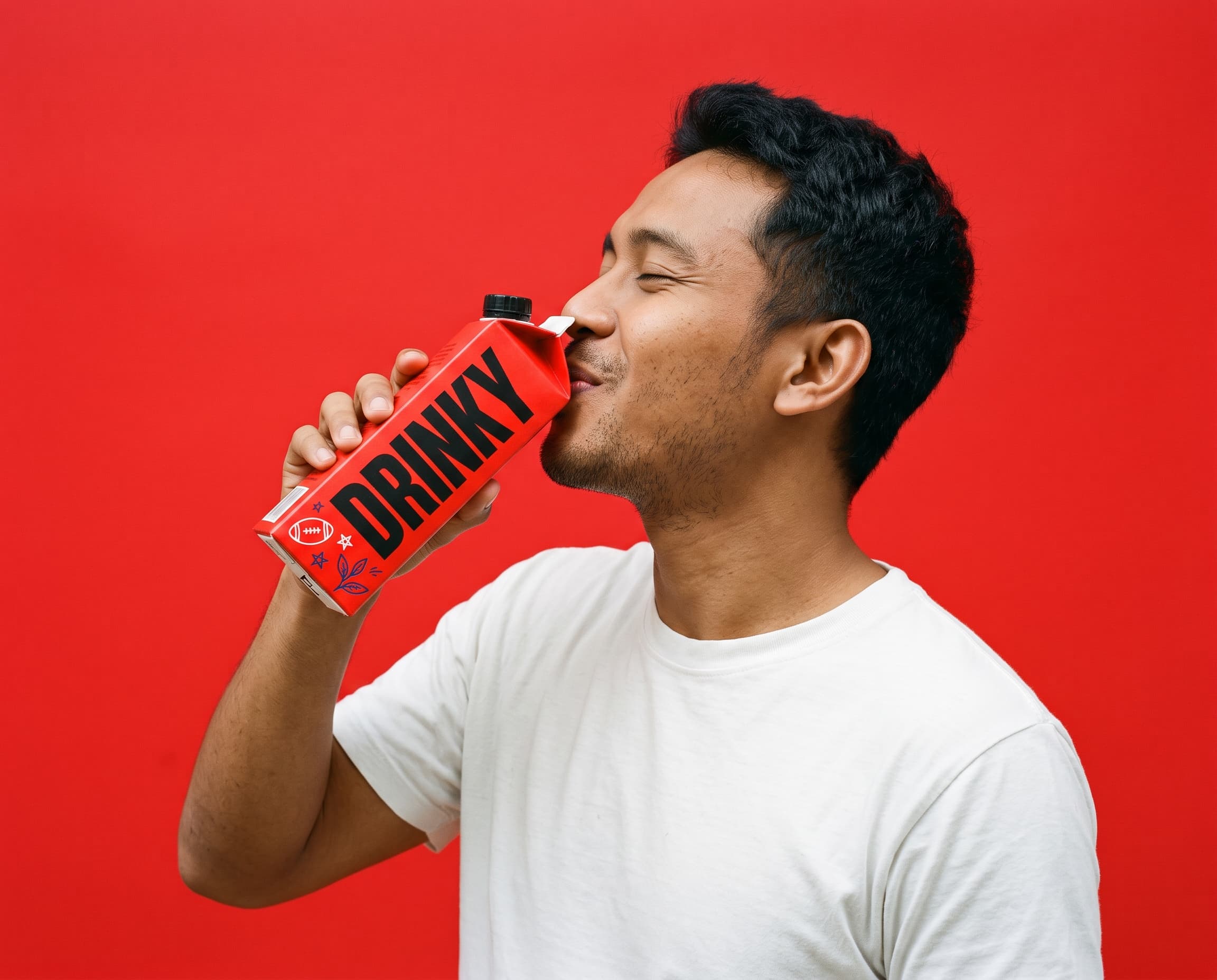 A young man in a white t-shirt drinking from a red DRINKY carton